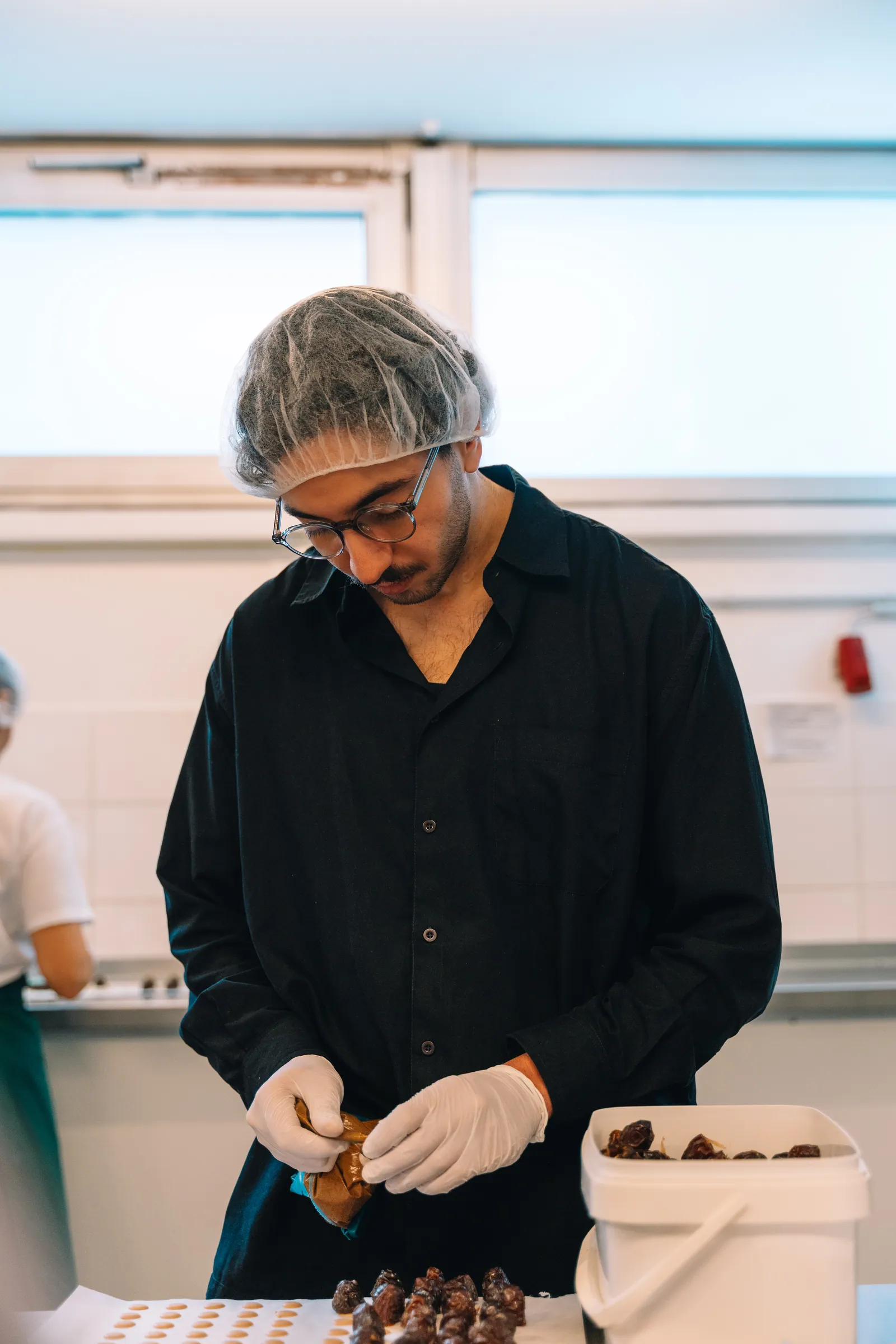 Anas Elimani mit Haarnetz probiert eine Praline in der Produktion von djoon.